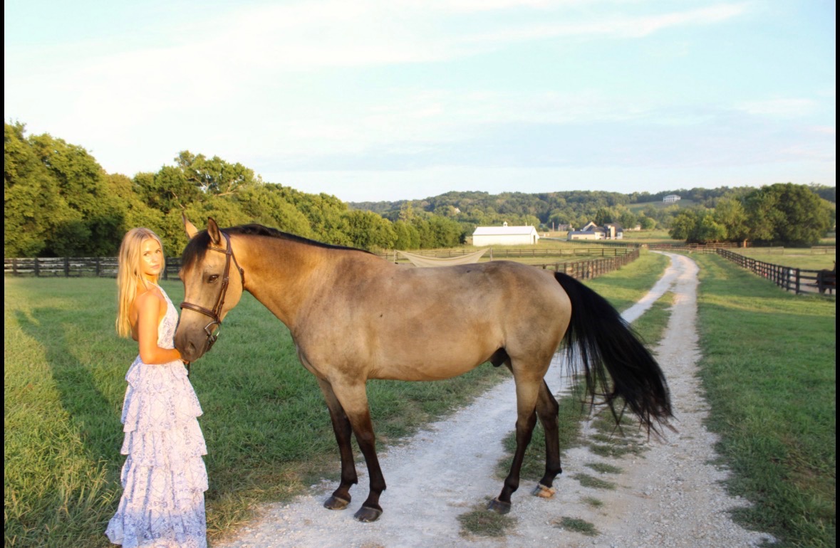 Young woman in a lace dress with a buckskin horse on a Tennessee farm lane at golden hour